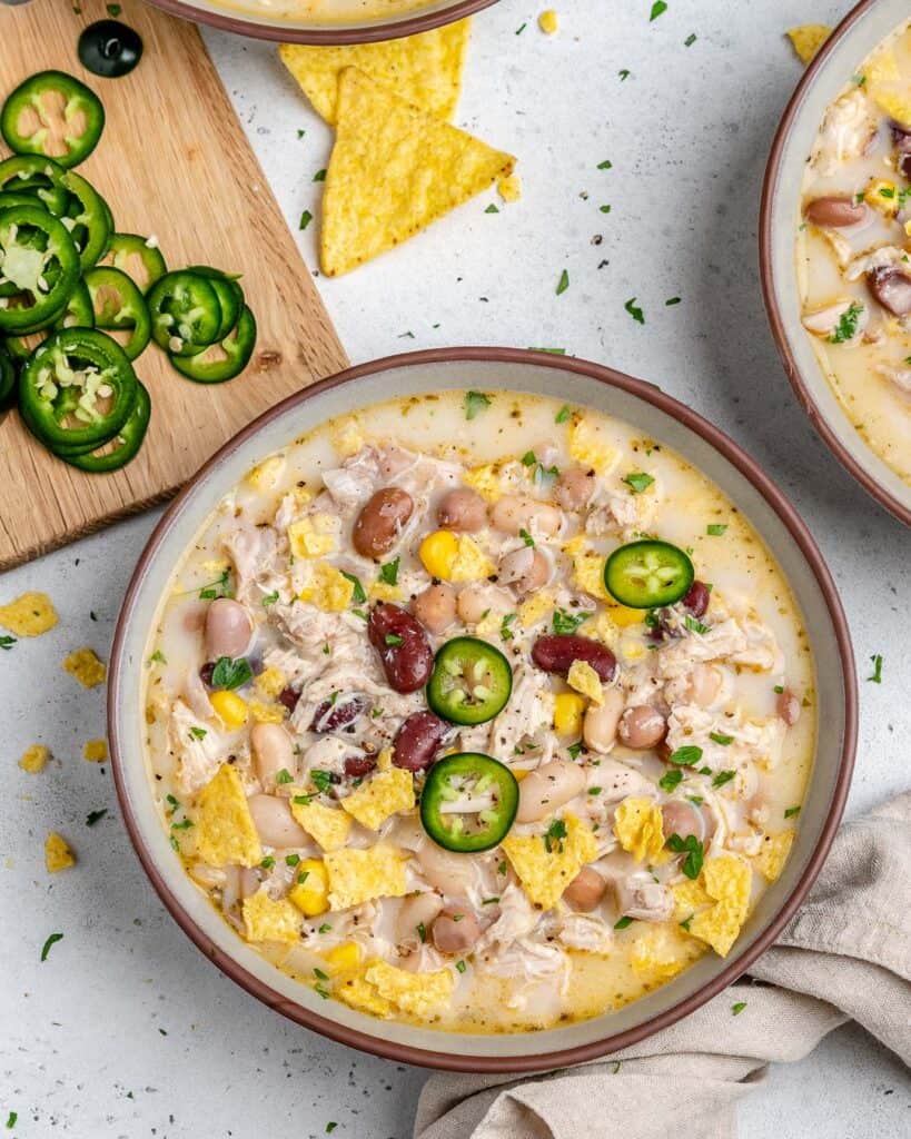 bowl of white chicken chili next to a cutting board with sliced jalapenos 