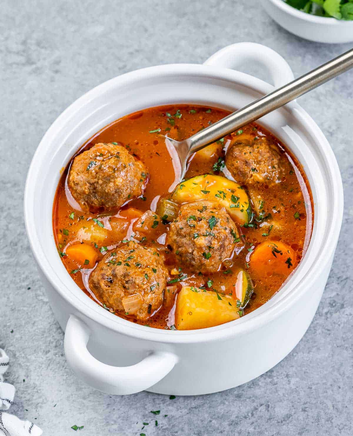 Spoon in a bowl of Albondigas Soup with meatballs and veggies.