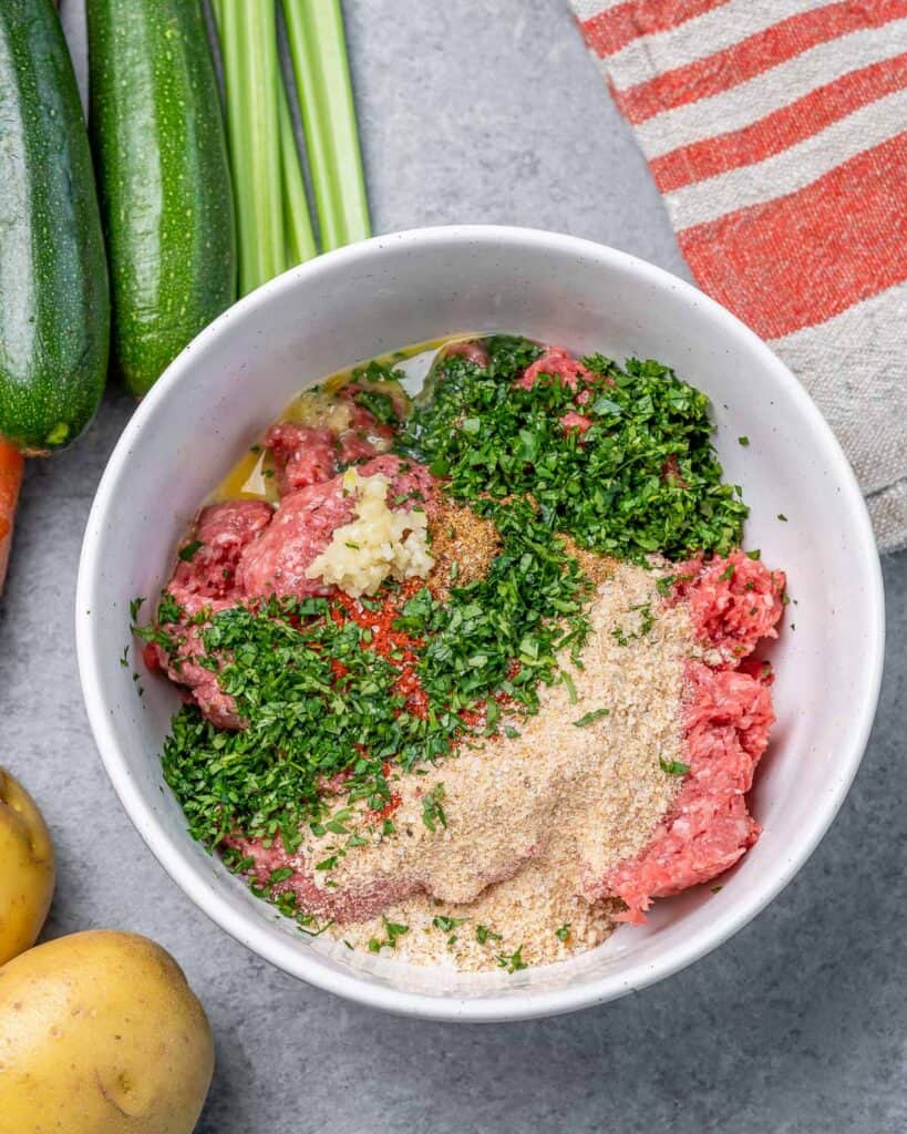 Mixing beef with herbs, breadcrumbs and eggs in a white bowl.