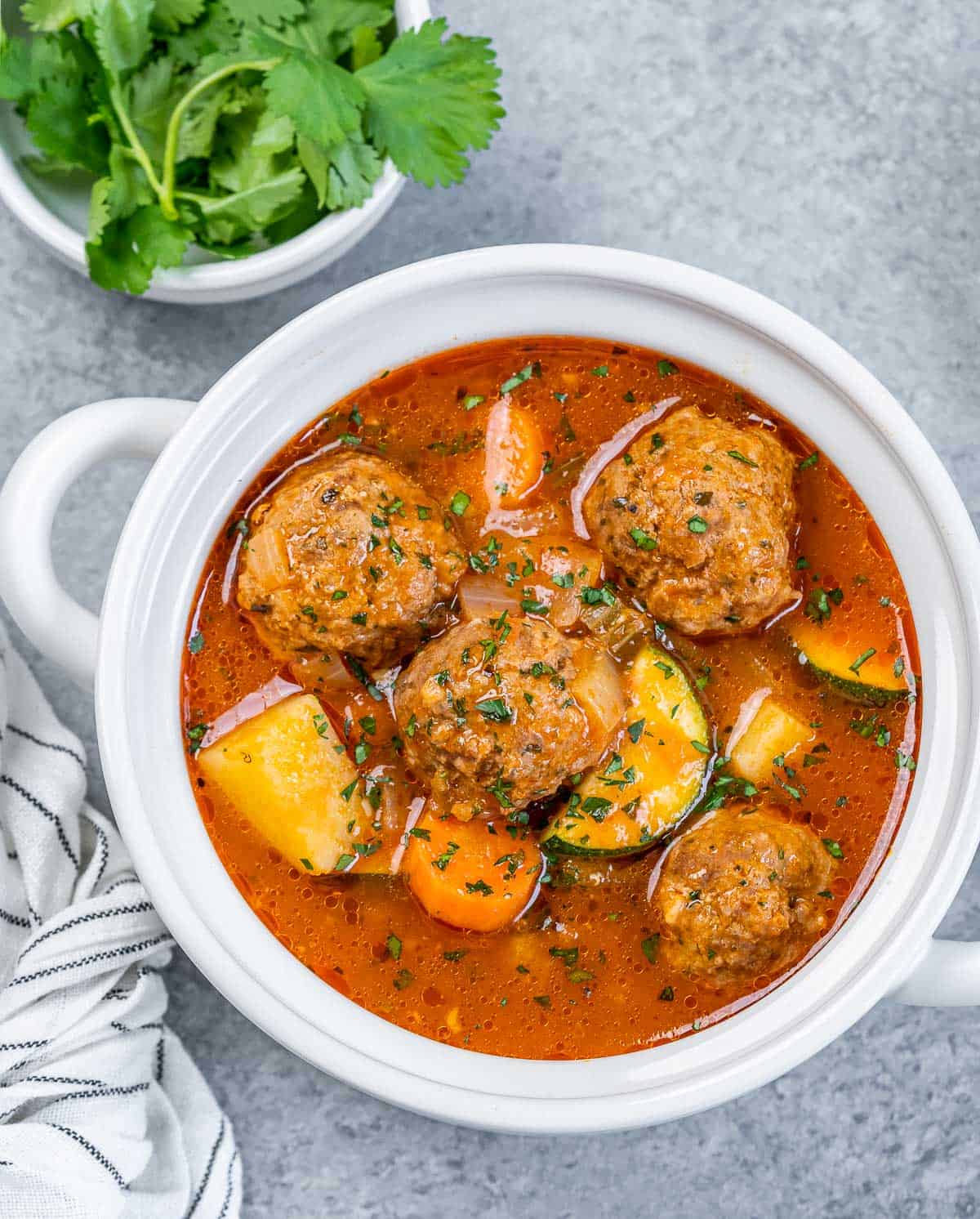 top view of a white bowl with handles that has Mexican meatball soup that is tomato based