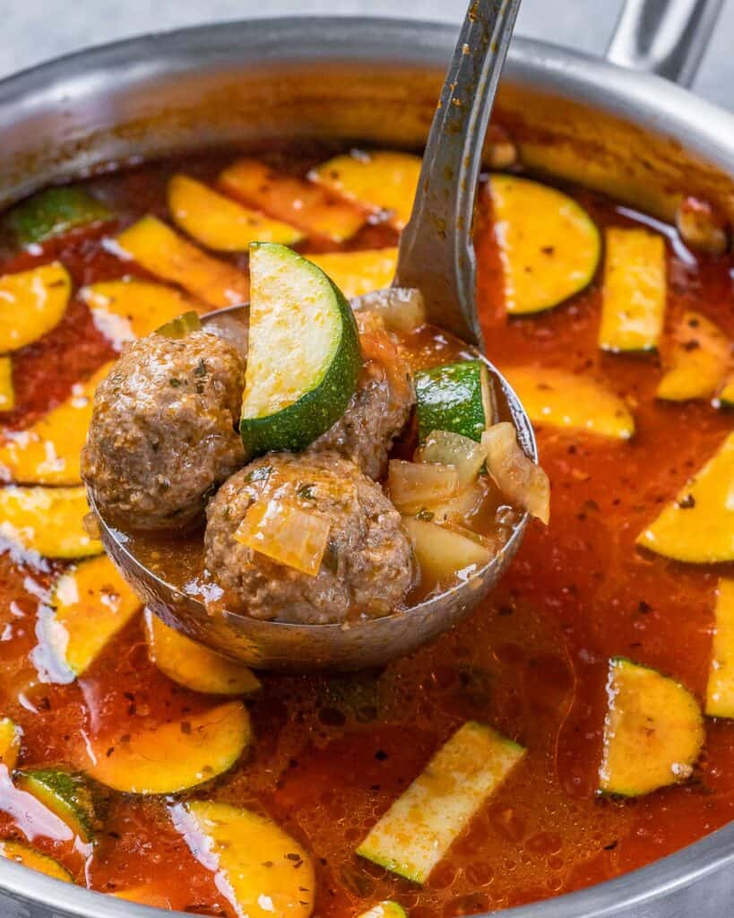 Ladling meatball soup out of a soup pot.