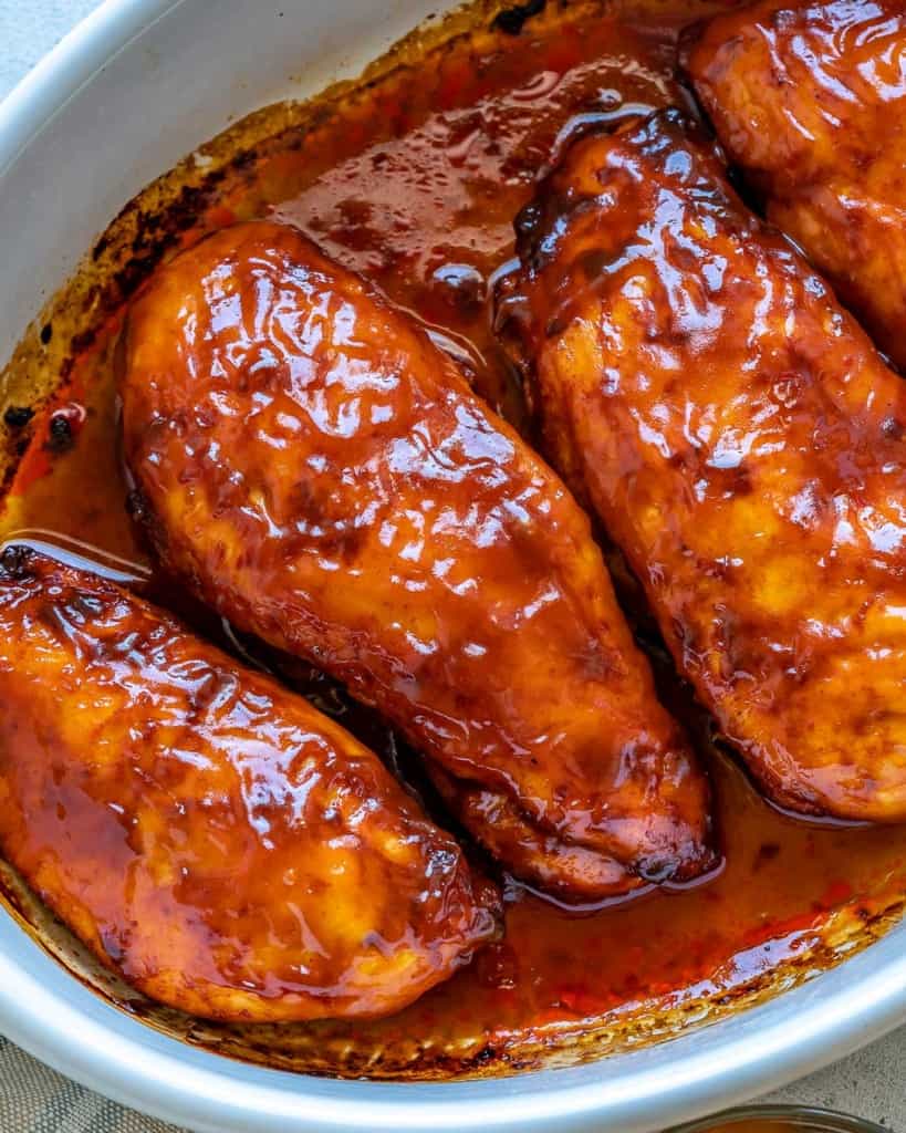 Top view 4 baked chicken breasts with bbq sauce in white baking dish