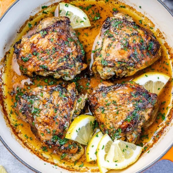 top view of 4 baked chicken thighs on a skillet with lemon wedges