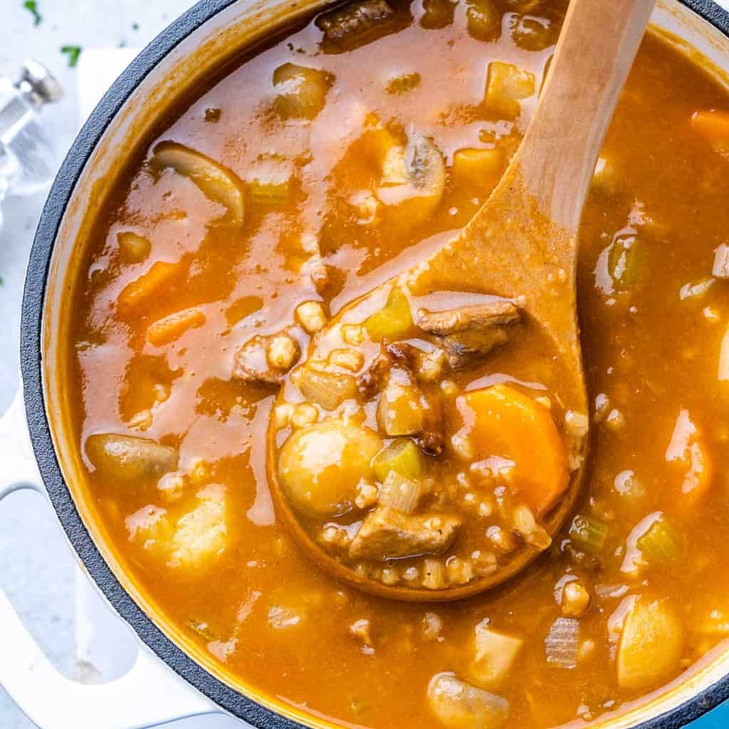 beef and barley soup in a pot with wooden spoonful of soup