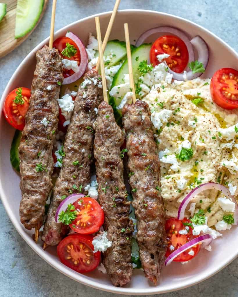 top view of 4 grilled kafta with hummus and veggies