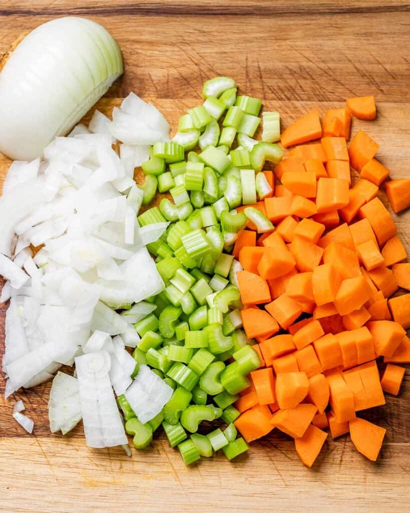 Onion, celery and carrots chopped on a cutting board.