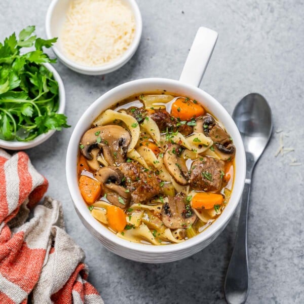 top view of a white bowl with beef noodle soup next to a small bowl of fresh parmesan cheese and fresh parsley