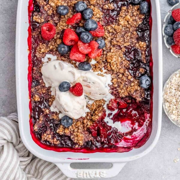 a white dish with berry cobbler topped with a bit of vanilla icecream.