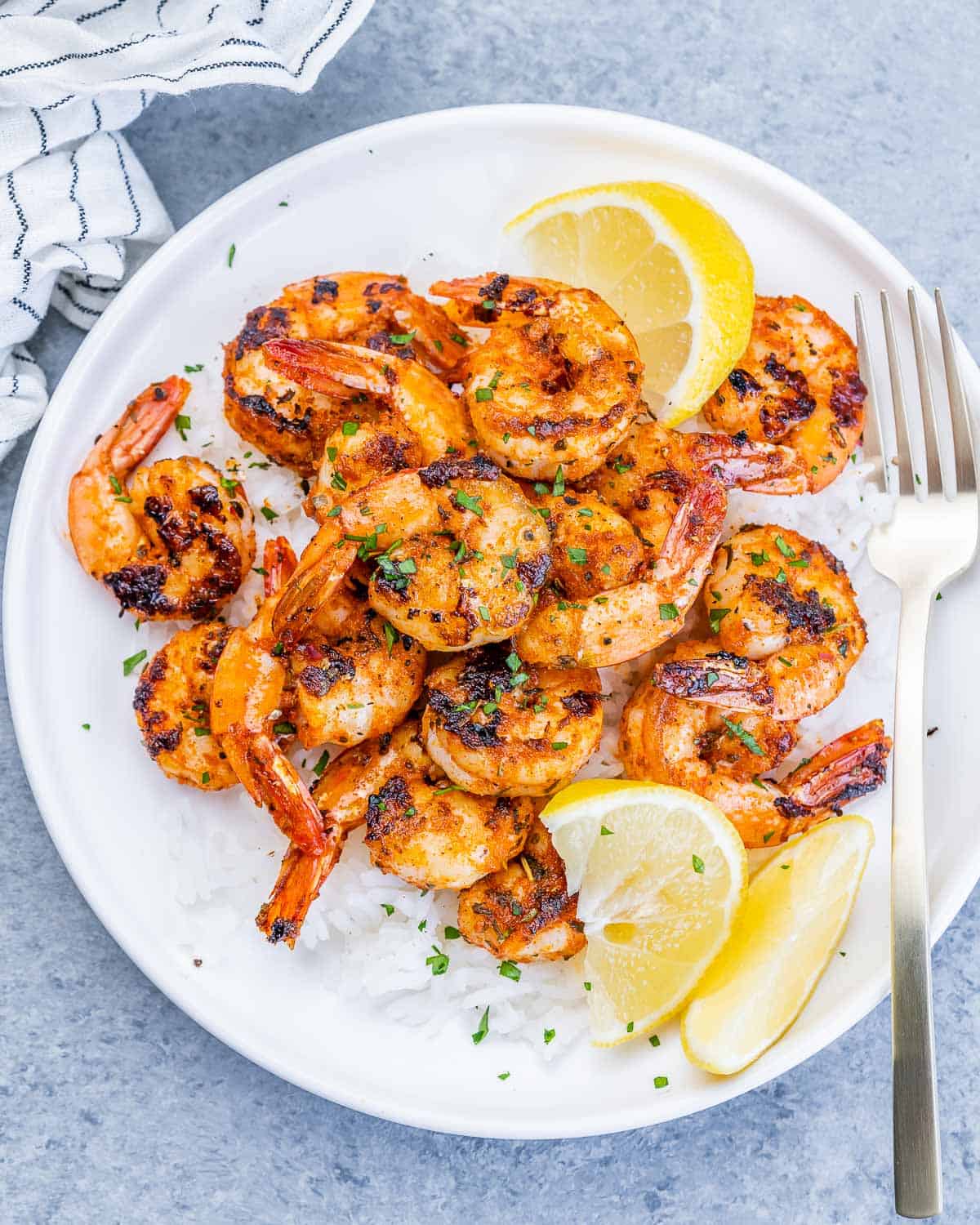 Top view of a round white plate with rice topped with blackened shrimp and lemon garnishes.