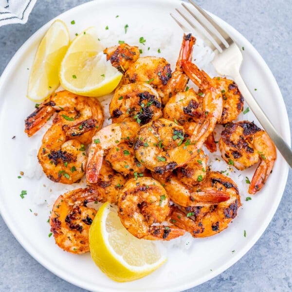 top view of a round white plate with rice topped with blackened shrimp and lemon garnishes