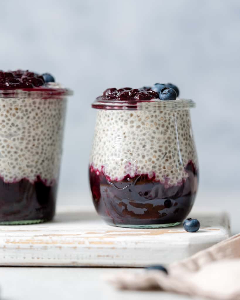Side shot of a jar with blueberry jam at the bottom of the jar and chia pudding on the top layer topped with more blueberries.