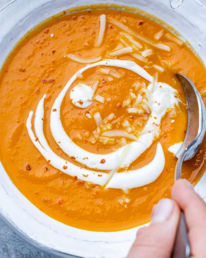 top view close up butternut squash soup in a white bowl with spoon in it topped with sour cream swirl