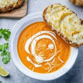 butternut squash soup in a white bowl with grilled cheesy bread over a bowl.