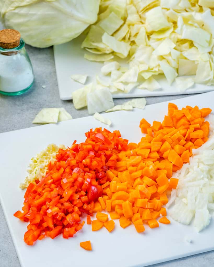 Carrots, onions, and bell peppers chopped on cutting board.