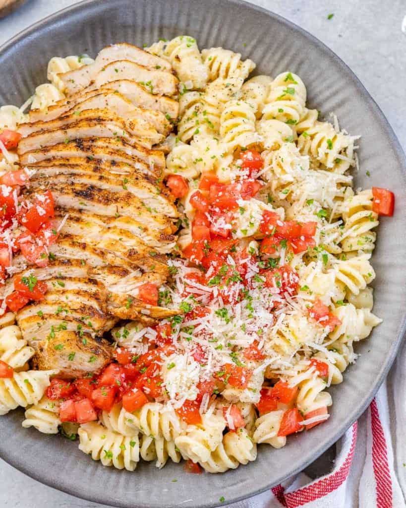 top view chicken pasta in a gray bowl topped with fresh tomatoes 