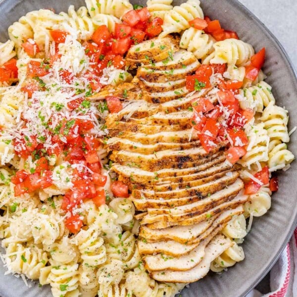 top view of pasta bowl with sliced cajun chicken breast, garnished with tomatoes and parmesan