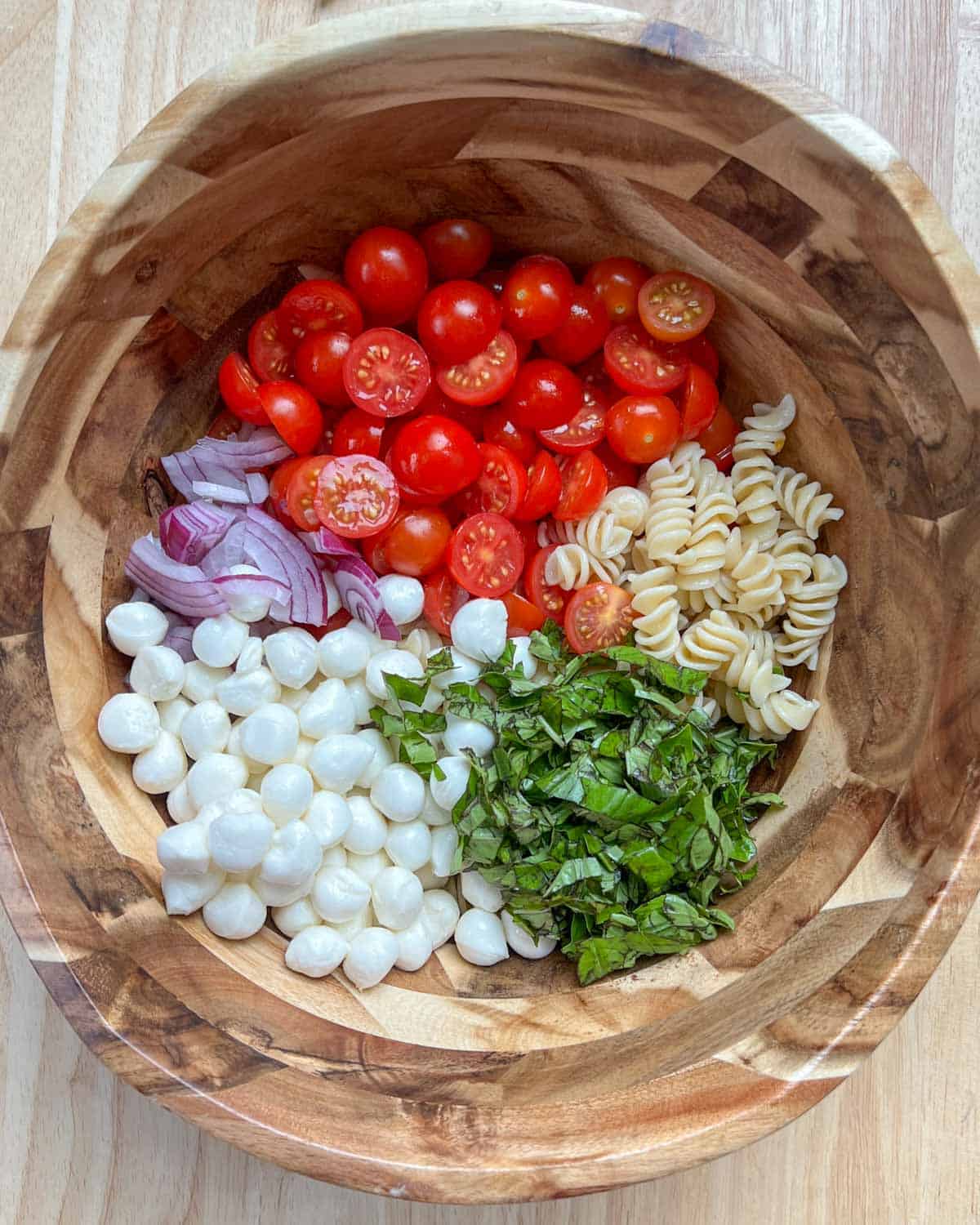 pasta, mozzarella cheese, sliced tomatoes, chopped basil, and sliced onions in a bowl.