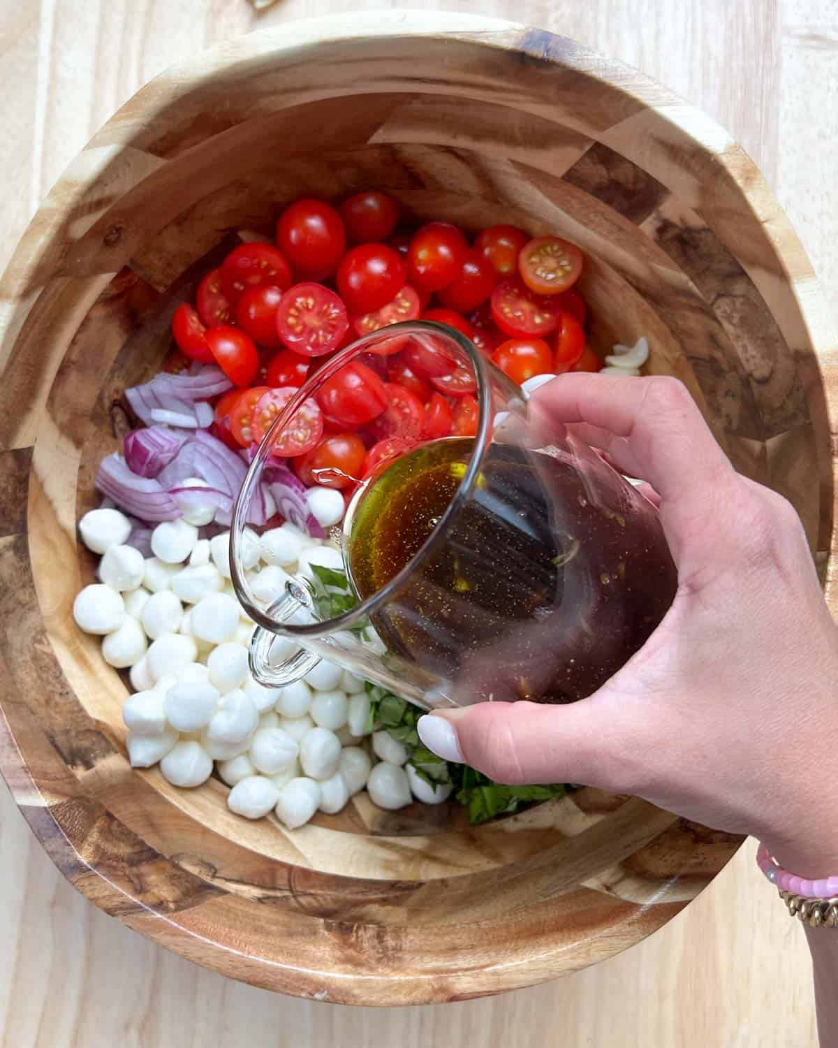 hand holding a jar with the dressing being poured over the salad bowl.