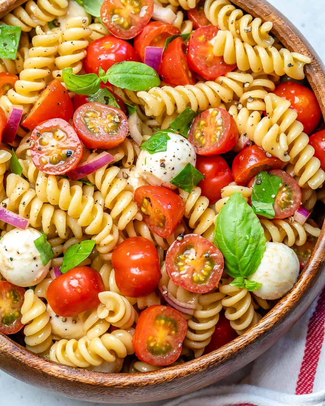 pasta salad in a round round bowl made with fresh chopped tomatoes, fresh mozzarella balls, and fresh basil.