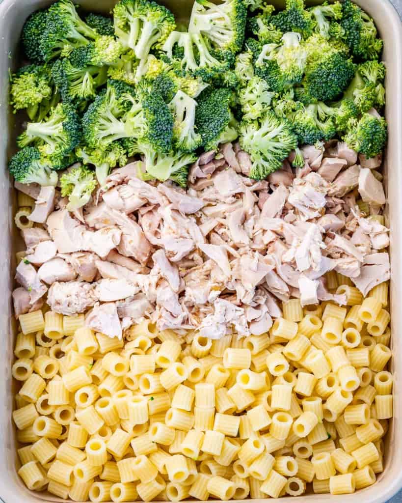 Pasta, broccoli florets and chicken added to a casserole dish.