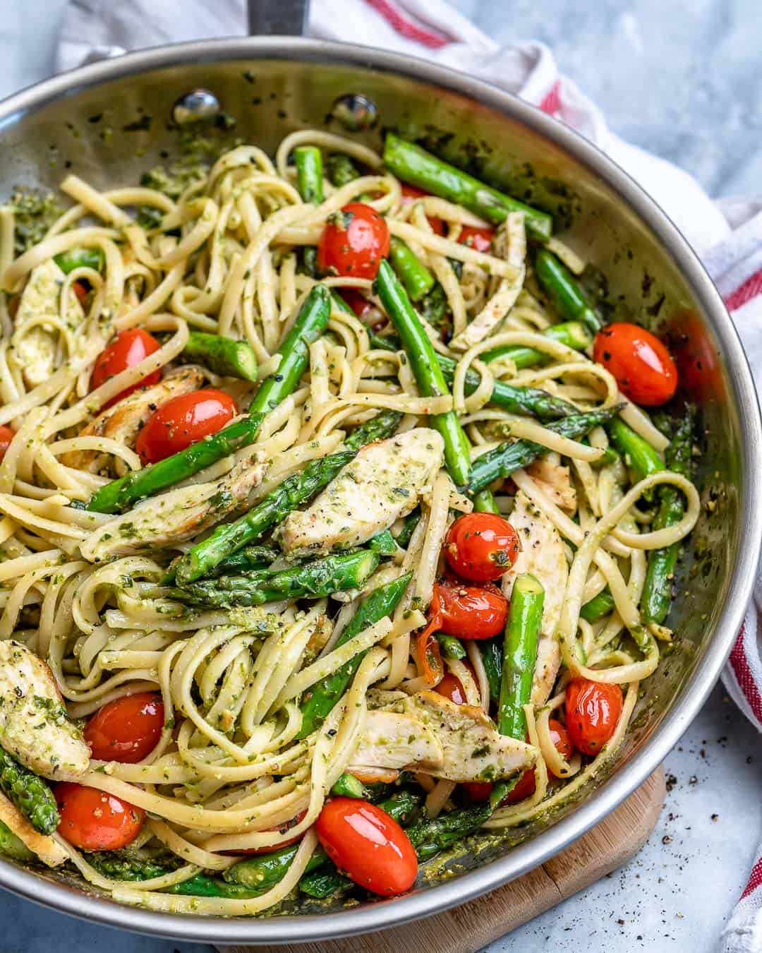 top view stainless steel skillet with green pesto-looking linguine pasta with chicken, asparagus, amd cherry tomatoes.