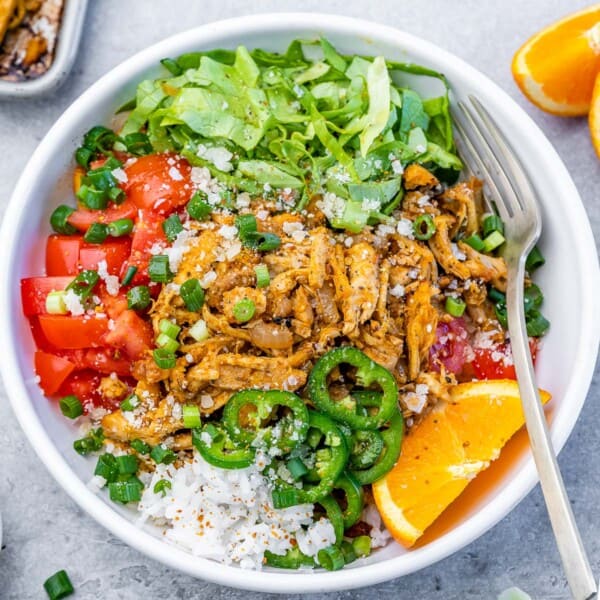 A round bowl with greens, rice, and tomatoes, topped with shredded chicken carnitas.