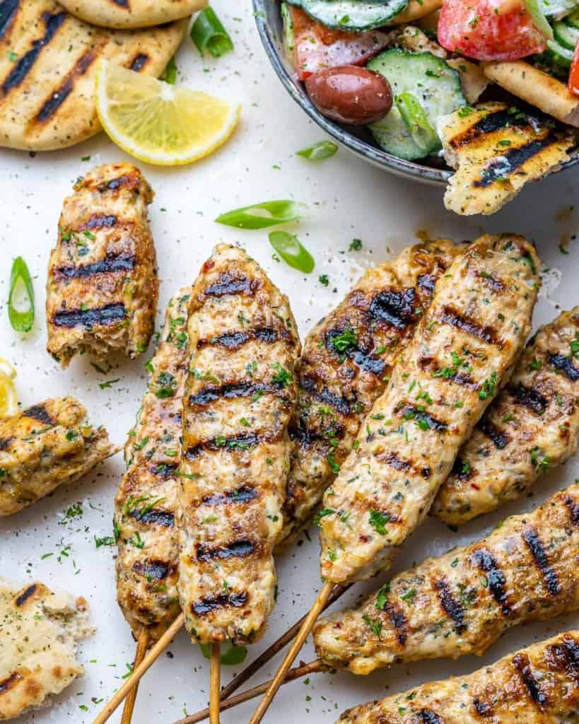 side shot of grilled chicken kafta kabob on a flat surface and lemon wedge on the top left corner 