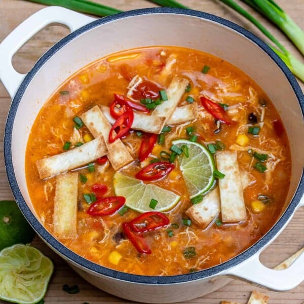white dutch oven that has chicken tortilla soup topped with tortilla and sliced lime.