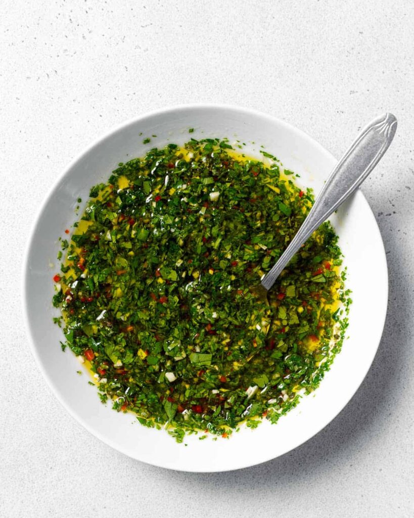 top view of a round white bowl with green chimichurri sauce  with spoon in bowl