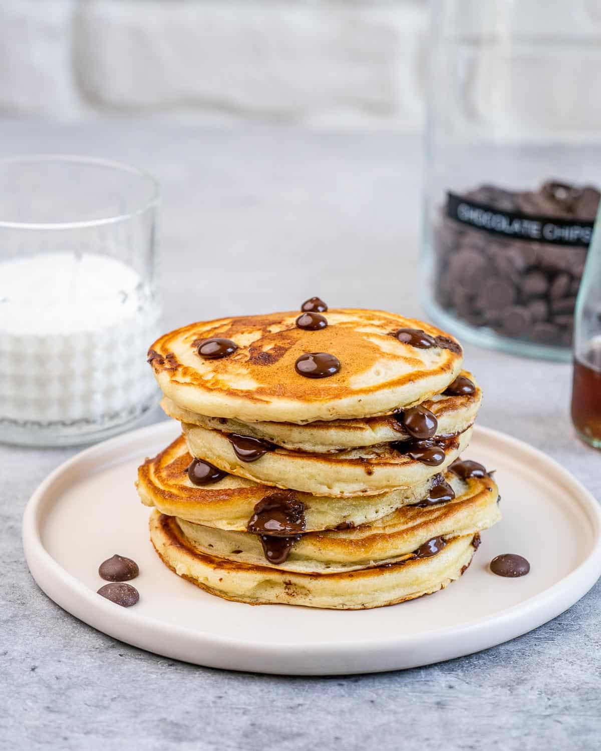 stacks of chocolate chip pancakes on a plate with a cup of milk next to the plate.