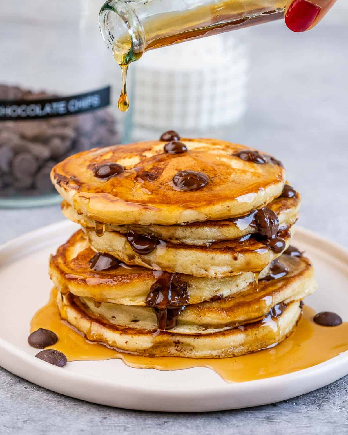 Drizzling maple syrup over the top of a stack of pancakes.