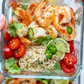 a meal prep bowl with sauteed shrimp, brown rice, and chopped tomatoes.