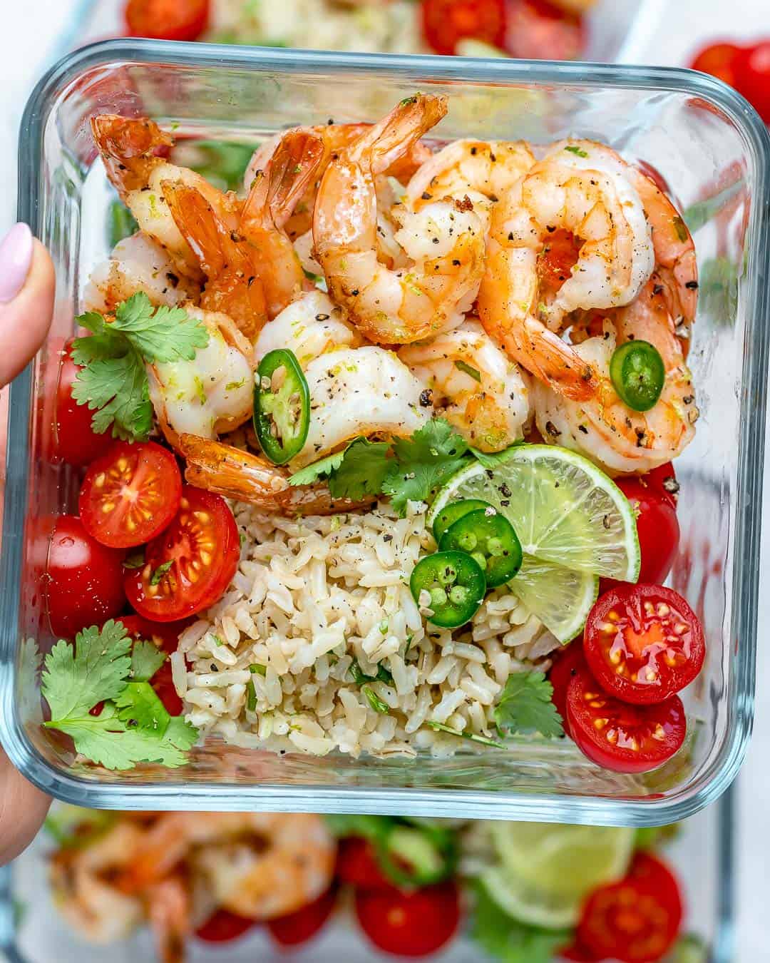 a meal prep bowl with sauteed shrimp, brown rice, and chopped tomatoes.