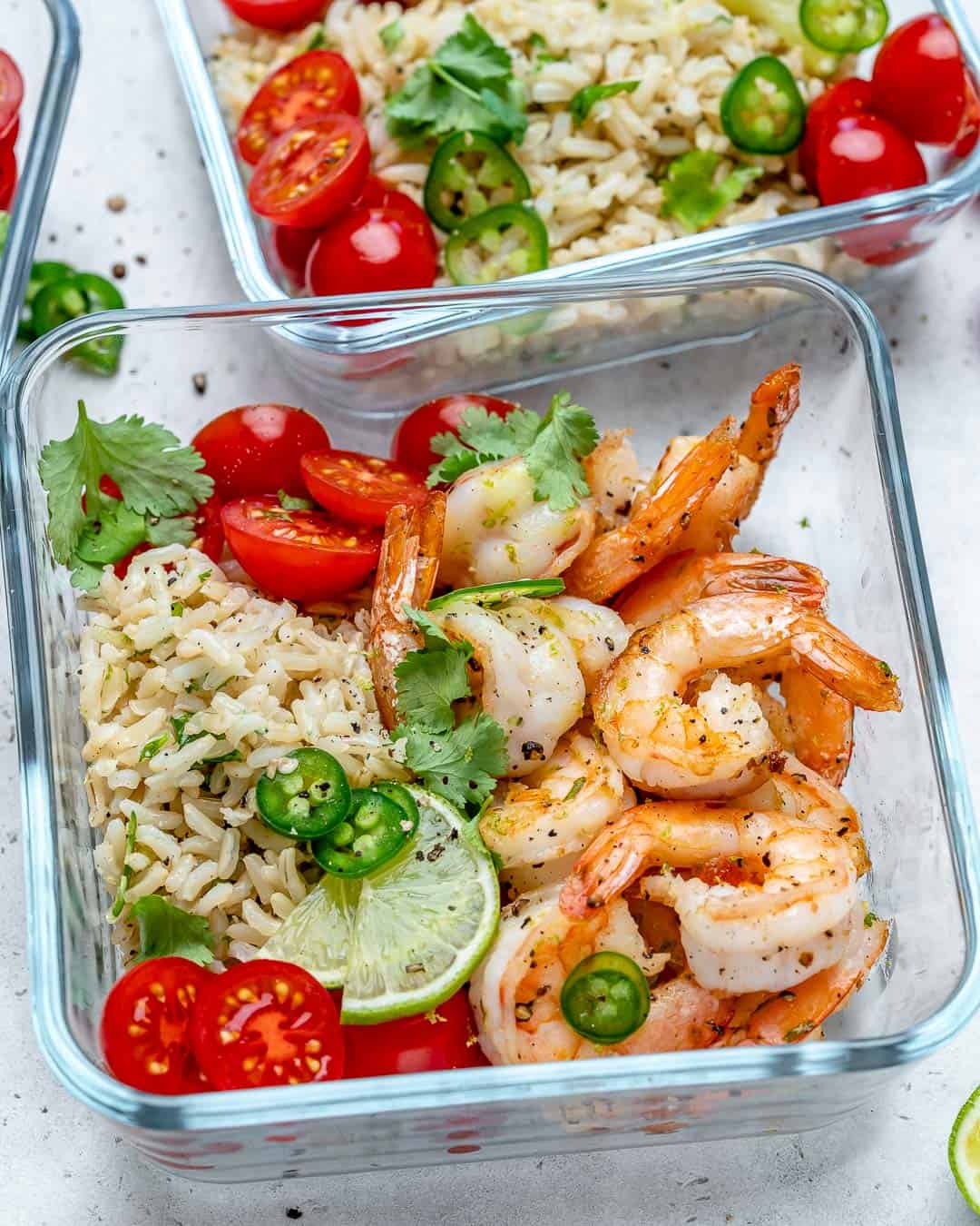 meal prep bowl with rice and sauteed shrimp, topped with lime wedge and chopped tomatoes.