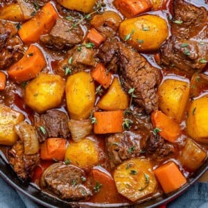 beef stew in a red and black skillet with potatoes and carrots.