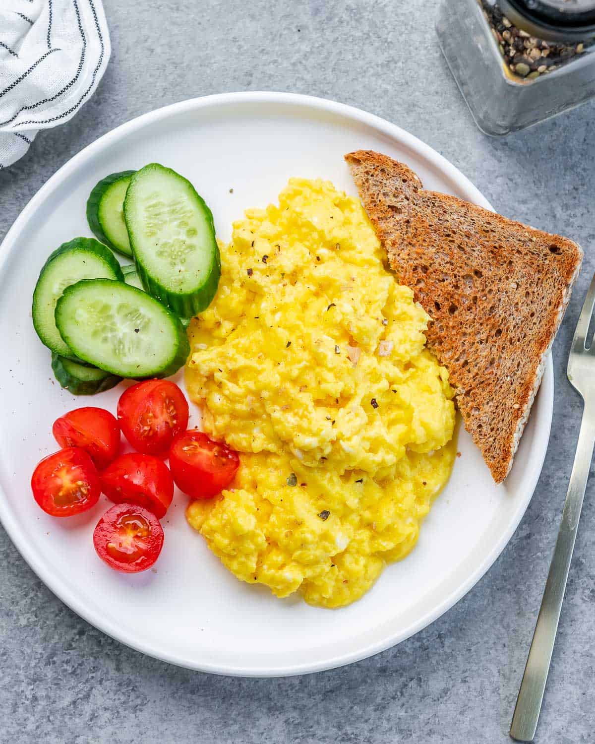 Top view of scrambled cottage cheese eggs with toast, chopped cherry tomatoes and sliced cucumber.