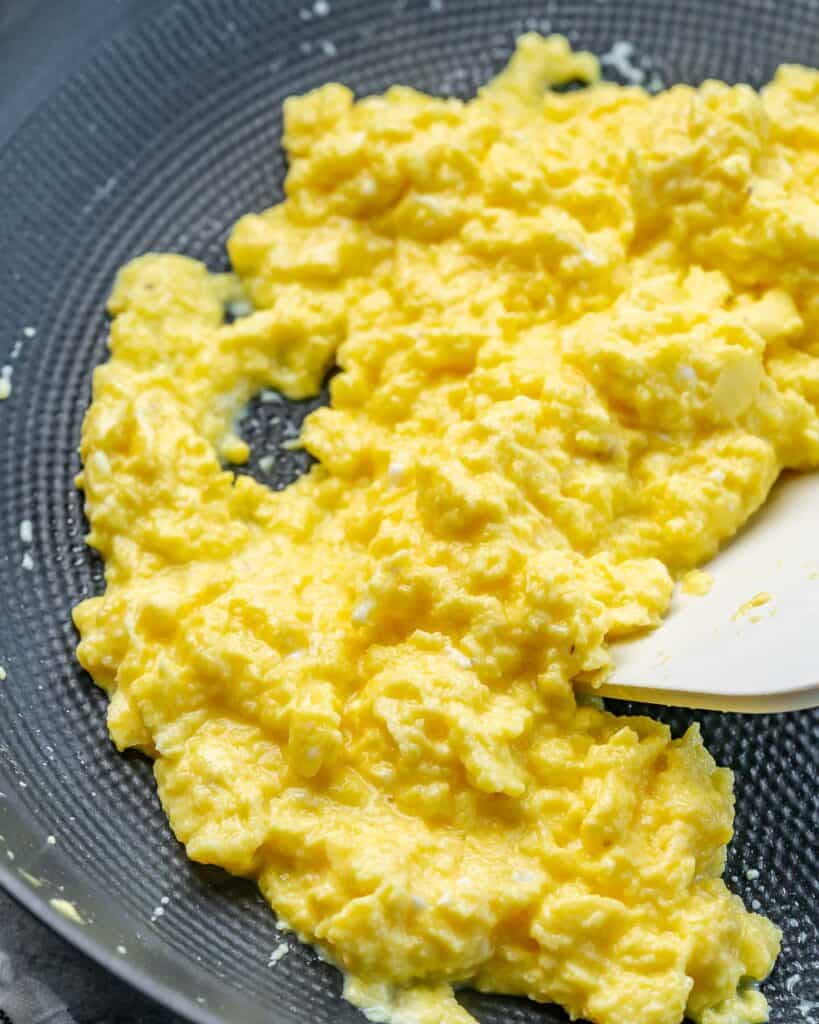 Using a spatula to cook eggs in a pan.
