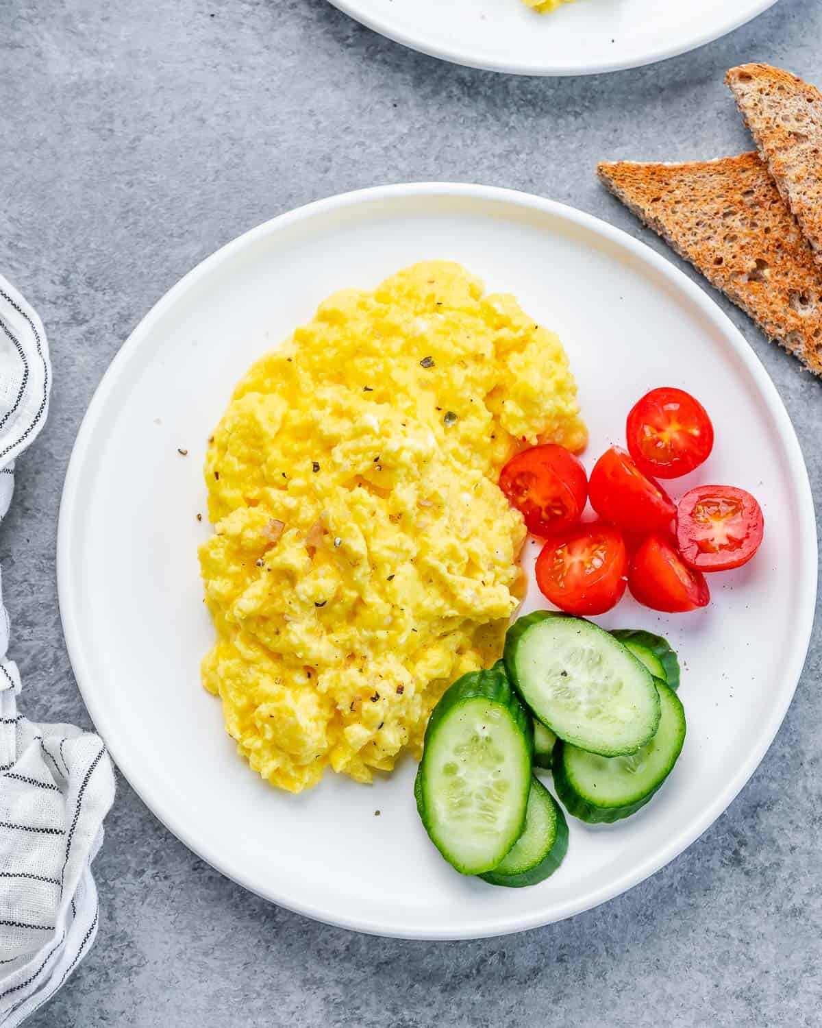 Cottage cheese eggs on a white plate with cucumbers and tomatoes.