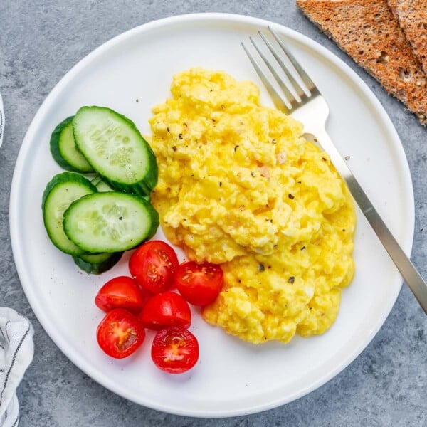 scrambled cottage cheese eggs with chopped cherry tomatoes and sliced cucumber on the left of the scrambled eggs.