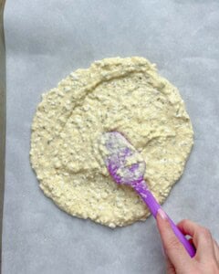 spatula spreading cottage cheese mixture into a round shape on a sheet pan.