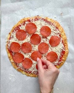 pepperoni being added to the pizza.