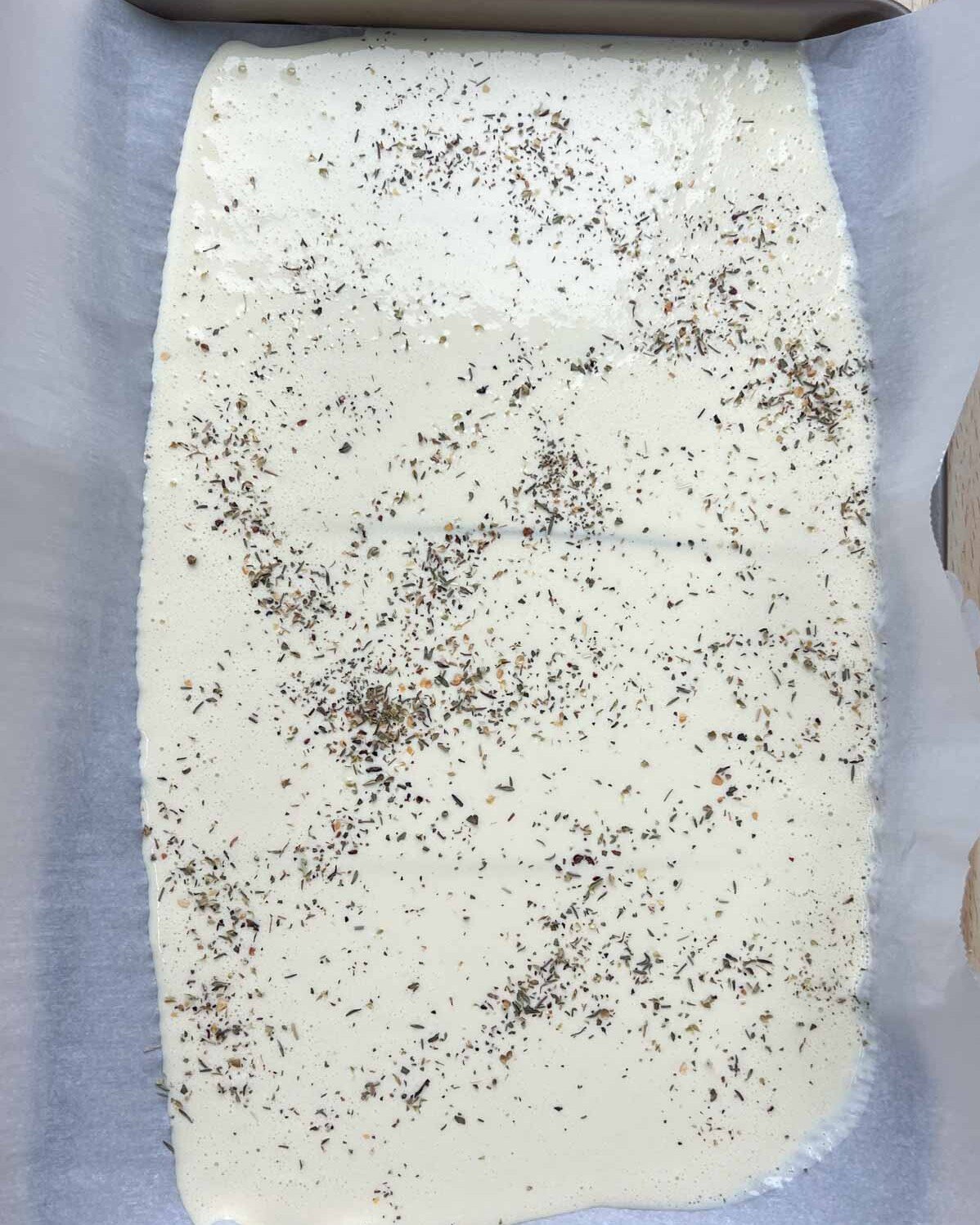 Italian seasoning is added over the cottage cheese batter over a sheet pan.