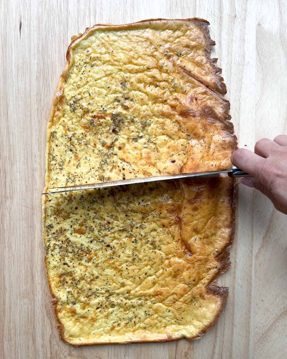 baked cottage cheese wrap on a cutting board with knife slicing it in middle.