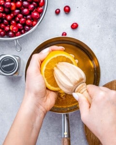 Squeezing fresh orange juice into a saucepan with maple syrup and orange zest.