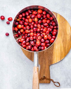 Cranberries in a saucepan with orange juice and maple syrup.