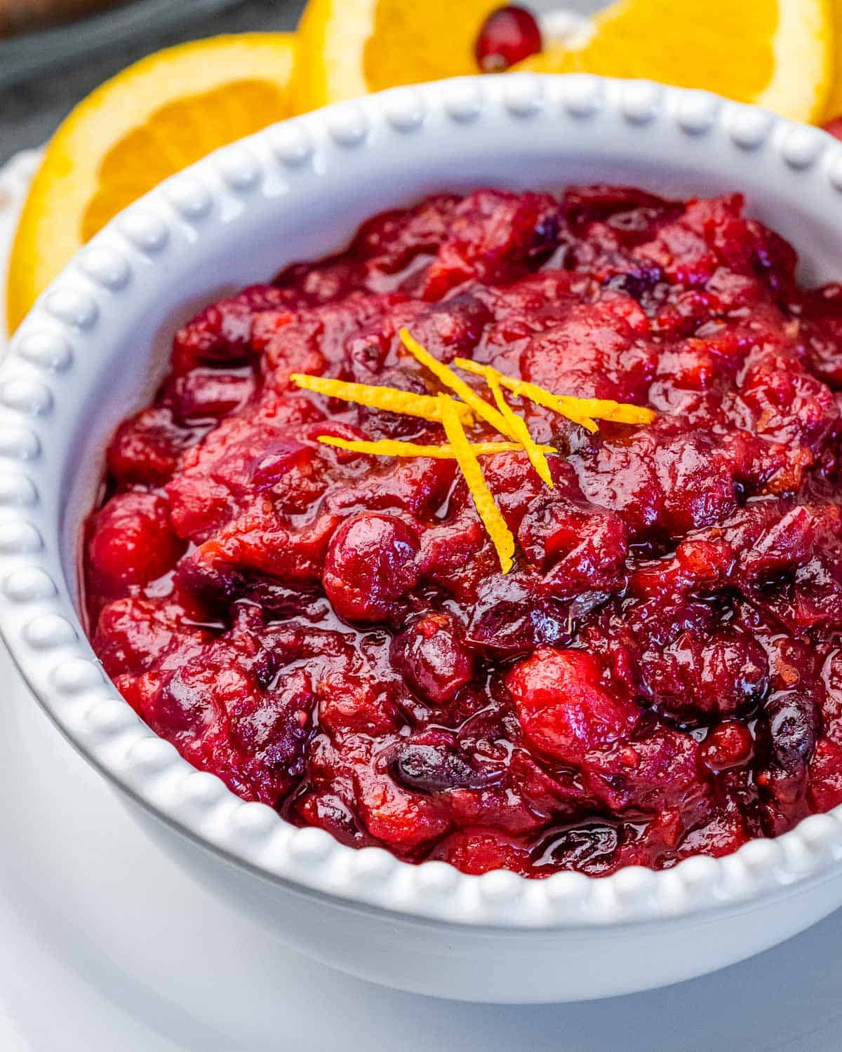 A white bowl with cranberry sauce topped with orange peel garnish.