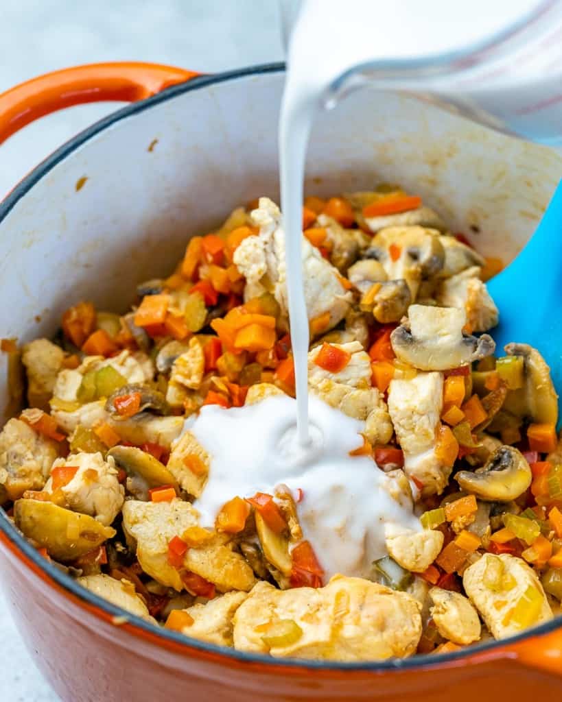coconut cream being poured in the pot of chicken and veggies 