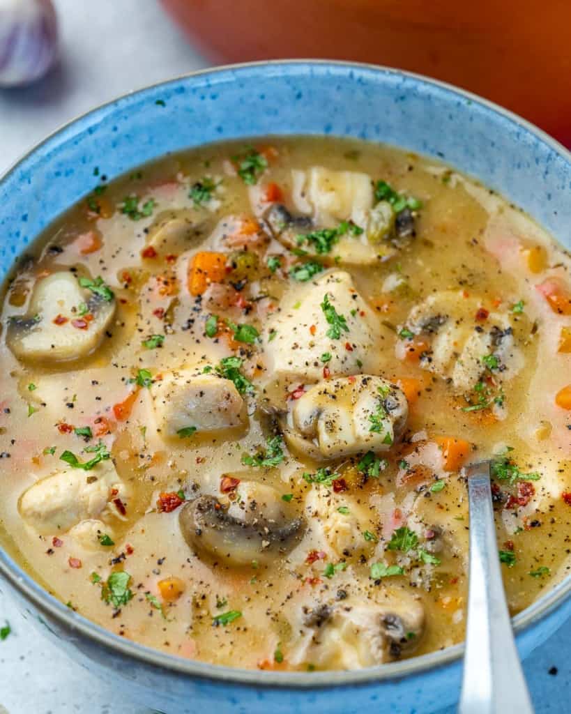 side shot of a bowl of chicken soup with spoon in it 