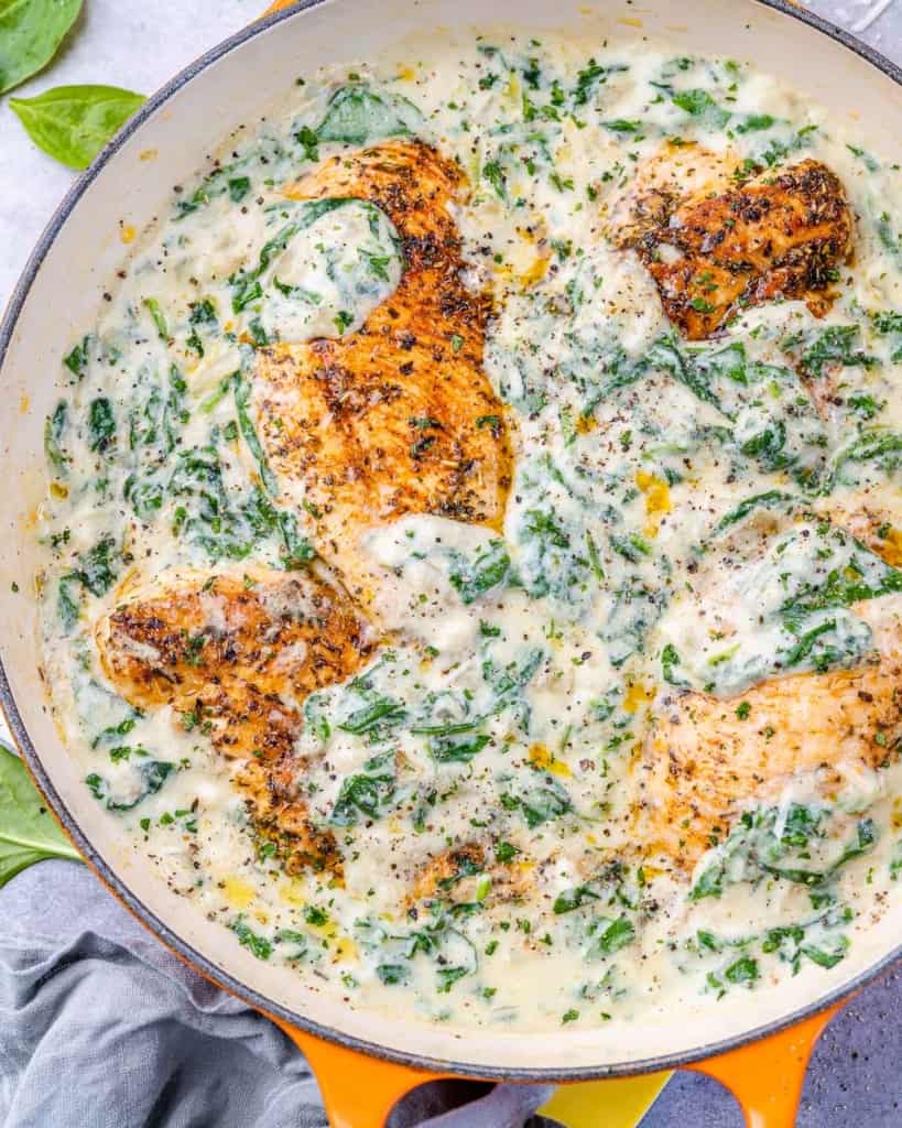 top view creamy chicken breast with spinach in an orange skillet