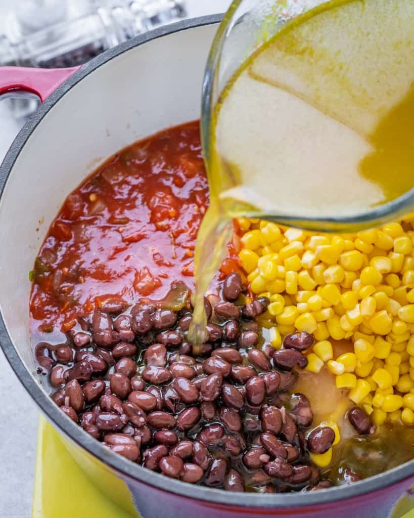 broth being added over veggies and beans in pot to make the tortilla soup